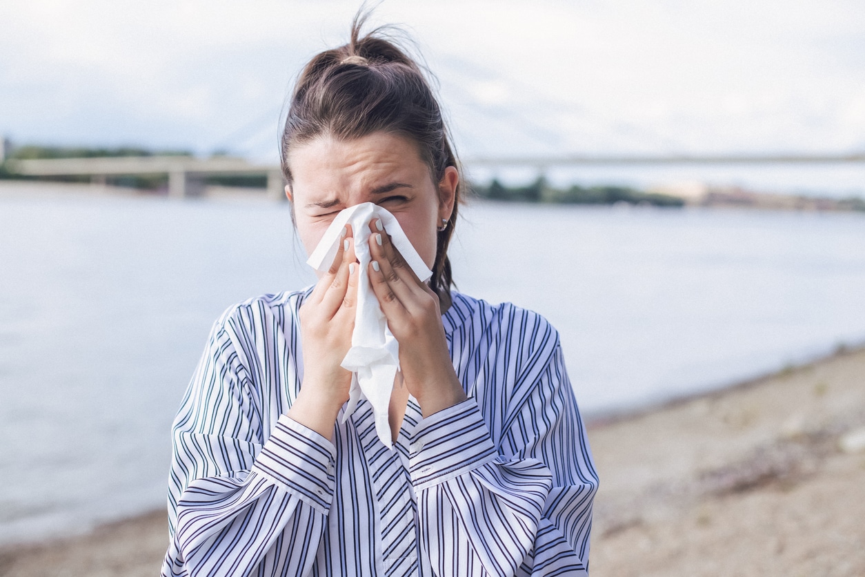 Woman on the beach blowing her nose.