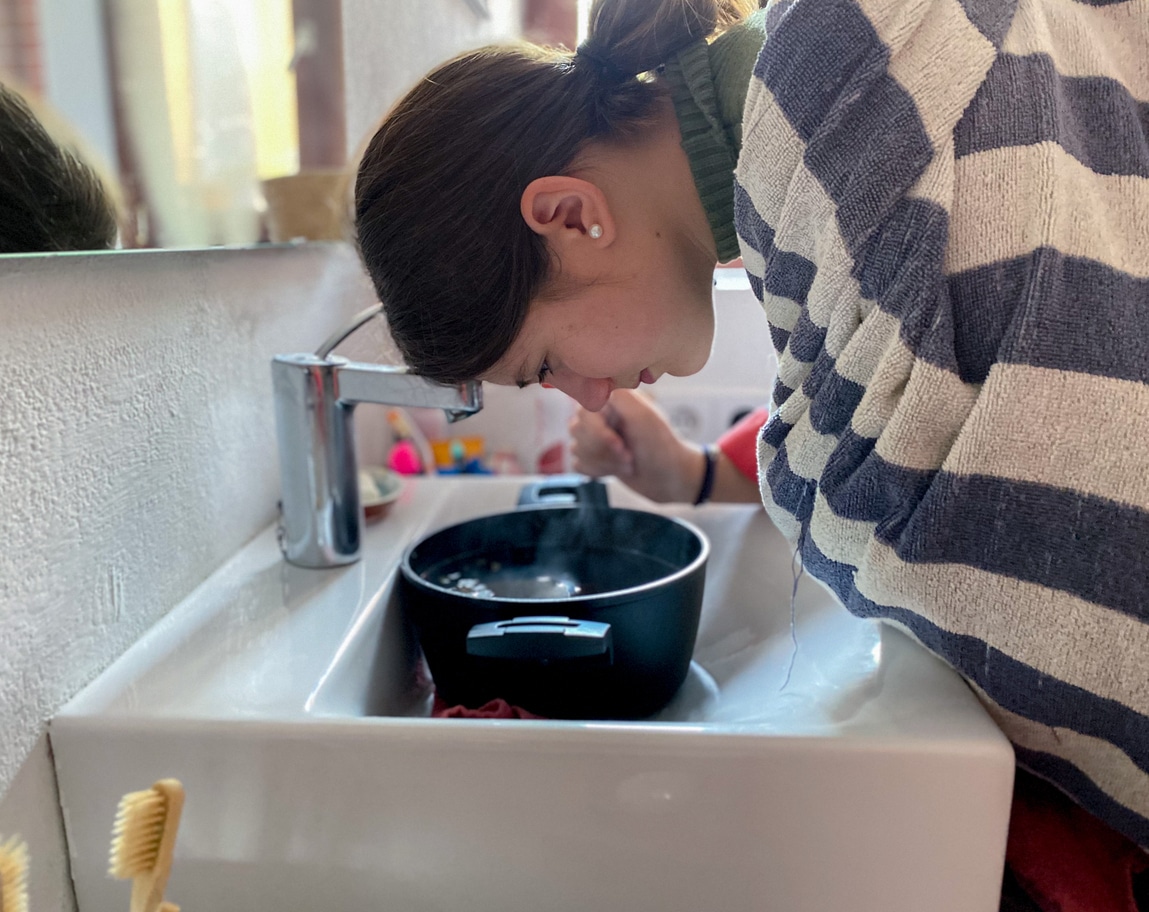 Woman with sinus pressure inhaling steam from a hot bowl of water.